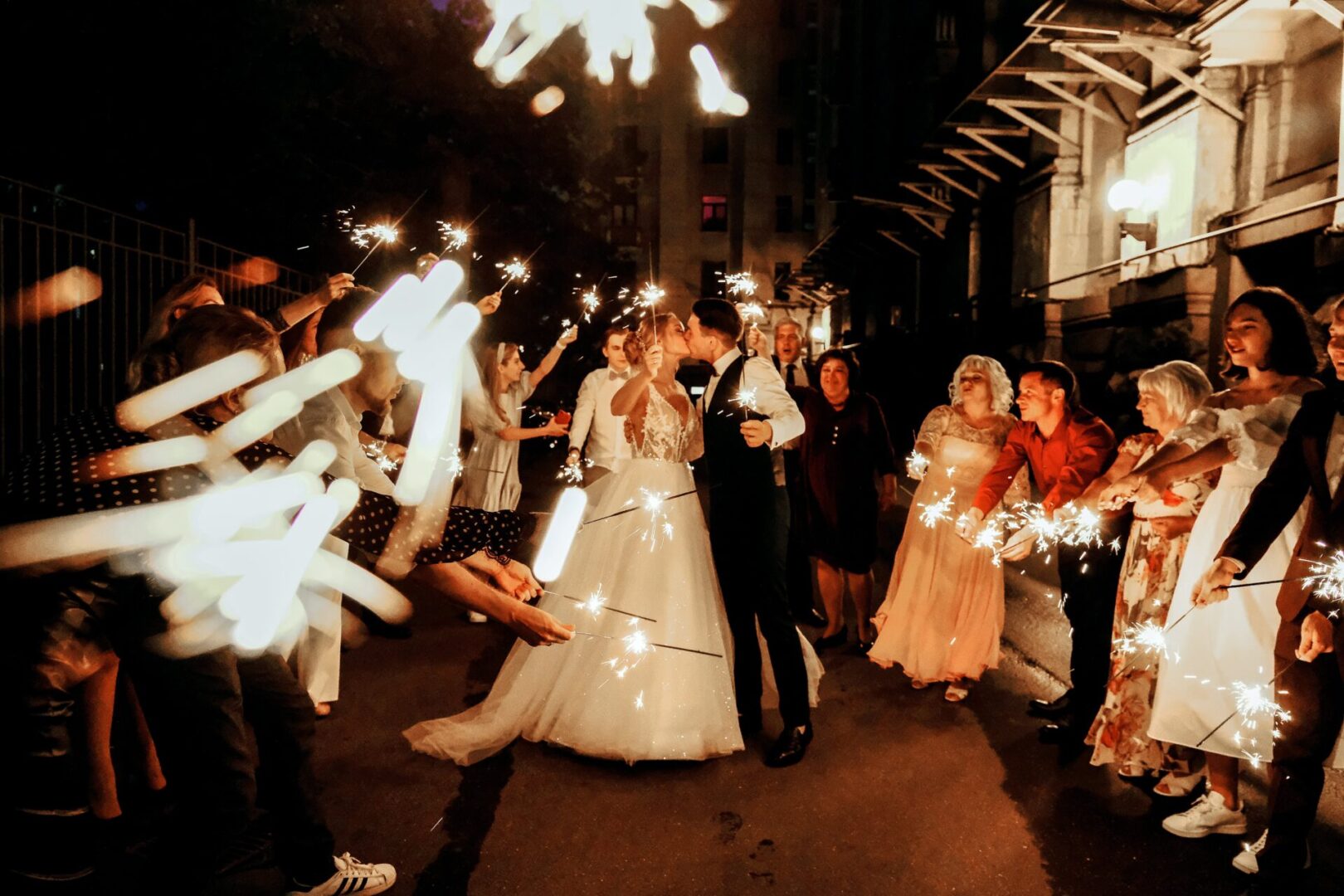 A bride and groom kiss as they walk through sparklers.